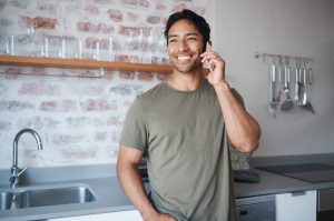 Happy, smile and man on a phone call in the kitchen of his home talking on technology for communica